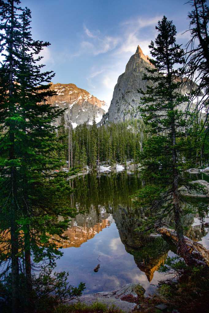 A river beside a mountain with talls trees.